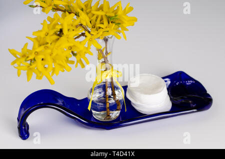 Cotton pads and yellow flowers on a blue plate made from bottle on white. Interior items concept . Makeup removal and skin care. Space for text Stock Photo