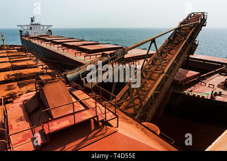 Port operations for managing and transporting iron ore. Unloading fines ore from TGV transhipper boat into hold of OGV ocean going vessel at sea Stock Photo