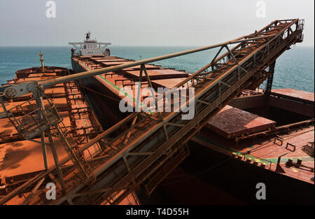 Port operations for managing and transporting iron ore. Unloading fines ore from TGV transhipper boat into hold of OGV ocean going vessel at sea Stock Photo