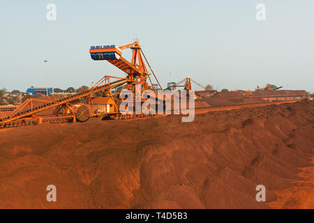 Port operations for managing and transporting iron ore. Over stock piles to stacker reclaimer & newly built stacker with Butterfly stacker in distance Stock Photo