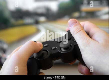 Man playing racing video game on TV. Gamepad controller in hands. Stock Photo