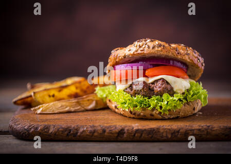 Home made hamburger with green salad and with american potatoes behind. Brown wooden background. Stock Photo