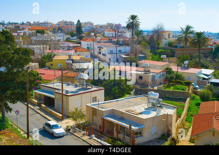 Aerial skyline of Paphos town in sunlight, car on road among houses of typical architecture, palms and green trees, Cyprus Stock Photo