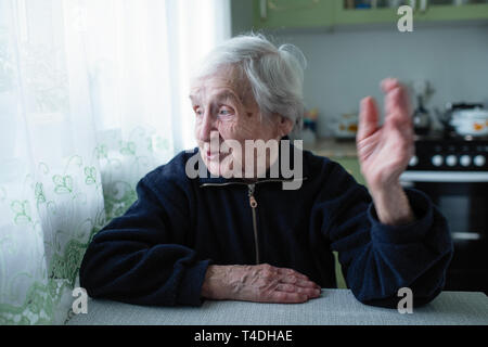 The old woman speaks expressively sitting at the table. Stock Photo