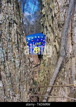 Iconic peace sign and Love as artistically hand painted on this rock wedged in a tree. Stock Photo