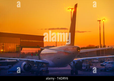 Commercial airplane parked in airport park at sunset. Orange red sky and copy space. Backlit sunset time. Refueling in taxi mode. Stock Photo