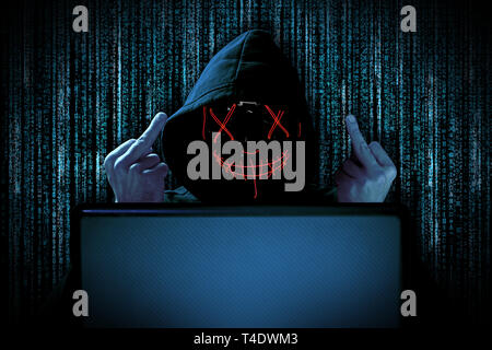 hacker with middle fingers gesture provocation red glowing mask behind notebook laptop in front of blue source binary code background internet cyber h Stock Photo