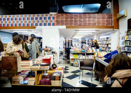 Athens, Greece - 26 Mar 2016: View from the street inside book store library with customers shopping for books at night  - beautiful Greek woman searching for new books to read Stock Photo