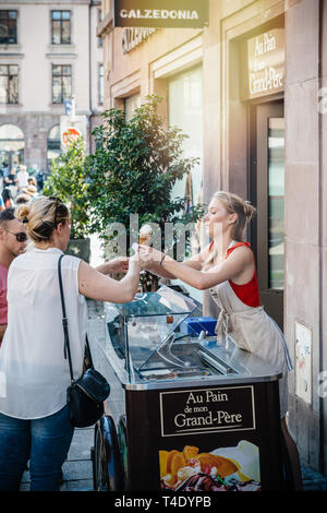 Strasbourg, France - Jul 22, 2017: Young blonde woman serving customer with french bio home-made - ice-cream parlor in central Strasbourg France  Stock Photo