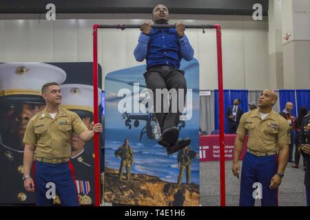 Marine Capt. Ethan Coots, officer selection officer with Officer Selection Station Lansing, and Staff Sgt. Douglas Weems, officer selection assistant, count pull-ups for Claude King, a senior at Hampton University, during a National Society of Black Engineers conference career fair in Detroit, Michigan, March 28. NSBE is holding its 45th annual national convention consisting of various programs and workshops that are designed to benefit grade school, collegiate, technical, professional and international attendees and the U.S. Marine Corps is a partner organization. Marines partner with organiz Stock Photo