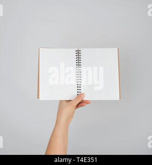 female hand holds open  notepad into a cell on gray background, copy space Stock Photo