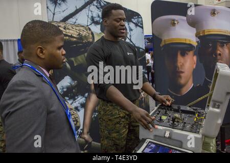 Marine Staff Sgt. Steven Bellamy, an explosive ordnance disposal technician with 2nd EOD Company, 8th Engineer Support Battalion, explains how to control EOD robots to Morayooluwa Ogunsina, a sophomore at Illinois Institute of Technology, during a National Society of Black Engineers conference career fair in Detroit, Michigan, March 29, 2019. NSBE is holding its 45th annual national convention consisting of various programs and workshops that are designed to benefit grade school, collegiate, technical, professional and international attendees and the U.S. Marine Corps is a partner organization Stock Photo