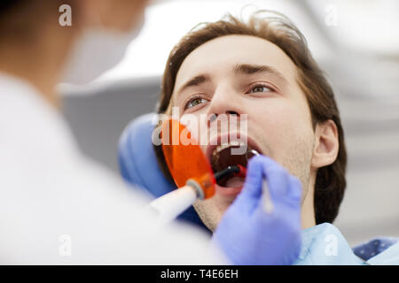 Unrecognizable dentist performing laser teeth whitening on man sitting in dental chair with mouth open, copy space Stock Photo