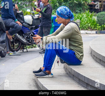 Singaporean man sitting on steps using his mobile telephone in Singapore. Stock Photo