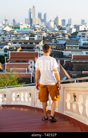 Man in orange shorts standing at the stairs of Golden Mount temple with his back to the viewer overlooking the city of Bangkok, Thailand. Vertical ori Stock Photo