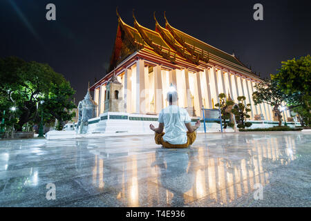 Man meditating in lotus pose in Wat Suthat Thepwararam at night, reflection in the floor marble tiles. Stock Photo