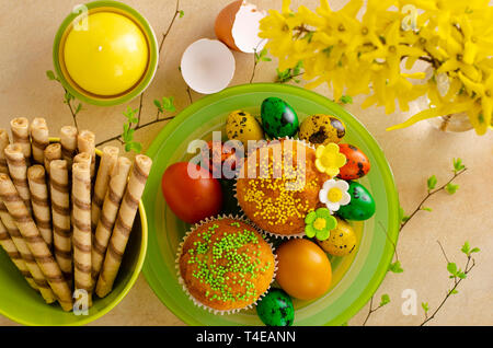 Muffins decorated with sprinkles, flowers of mastic, colored easter quail eggs on a kitchen table. Happy Easter holiday and greeting card concept. Top Stock Photo