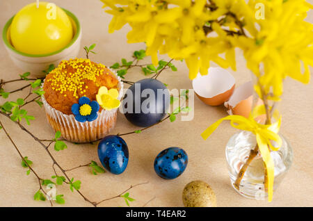 Muffins decorated with sprinkles, yellow flowers of mastic and blue easter quail eggs on pastel blue background. Top view. Easter Holidays and greetin Stock Photo