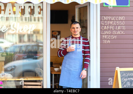 Happy small cafe owner standing at entrance holding takeaway coffee Stock Photo