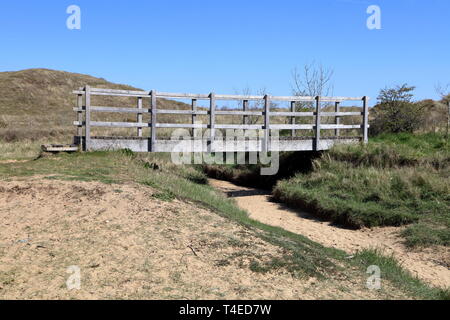 A fairly large wooden footbridge crossing a dried up sandy bottomed creek beside the tidal river Ogmore where this area tidally floods. Stock Photo