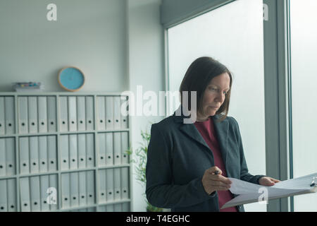 Concerned businesswoman reading business report papers in office, financial data analysis and strategic operations planning concept Stock Photo