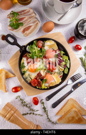 Fried bacon and eggs with topped camembert in iron pan Stock Photo