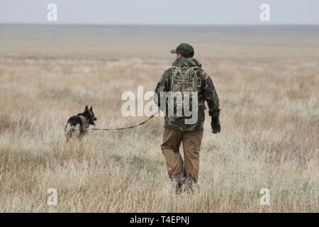 U.S. Air Force Staff Sgt. Antonio Padilla, 366th Security Forces Squadron military working dog trainer, and Alf, 366th SFS military working dog, act as opposition forces and hunt down “crashed” pilots during a combat search and rescue exercise April 2, 2019 at Saylor Creek Range near Mountain Home Air Force Base, Idaho. This is one aspect of the Gunfighter Flag exercise that tests the abilities of pilots to stay hidden until rescue arrives while military working dog trainers and their dogs hone their tracking ability in an expansive environment. Stock Photo