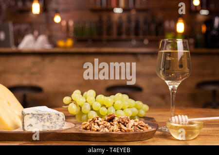 Food composition with varisious snacks for white wine on a wooden table. Fresh grapes. Walnuts on rustic plate. Stock Photo