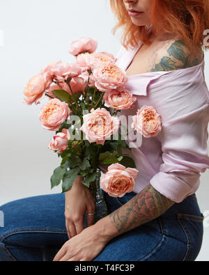 A bouquet of pink roses in a vase holds a girl with a tattoo on a gray background with copy space. St. Valentine's Day Stock Photo