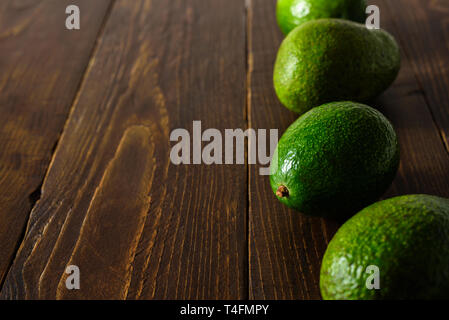 Avocados in row on dark wooden background. Text space Stock Photo