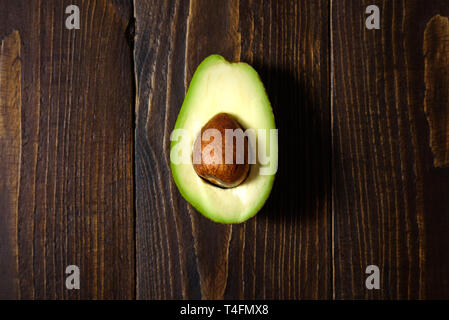 Avocado half on dark wooden background. Central conposition, hard light Stock Photo