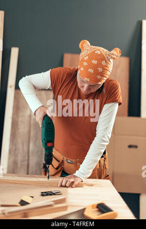 Female carpenter using electric drill in woodwork carpentry workshop, selective focus Stock Photo