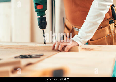 Female carpenter using electric drill in woodwork carpentry workshop, selective focus Stock Photo