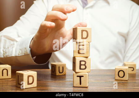 Businessman removes wooden blocks with the word Debt. Reduction or restructuring of debt. Bankruptcy announcement. Refusal to pay debts or loans and i Stock Photo