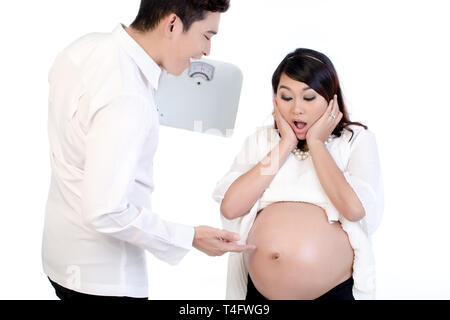 Man holding weigh scale pointing finger at his pregnant wife's belly Stock Photo