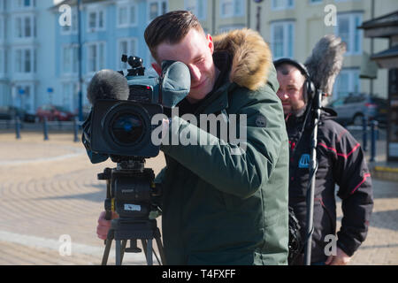 Media workers in the UK: A professional television crew  on location recording an item for broadcast, with the video camerman pointing his lens directly at the subject. UK Stock Photo