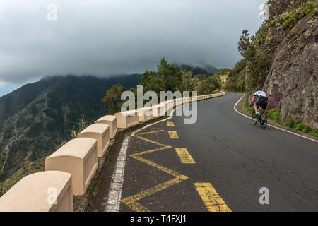 Dramatic mountain view of a cyclist on a road bike under the cloud in the Parque Rural de Anaga park, on the TF-12 road, Tenerife Stock Photo