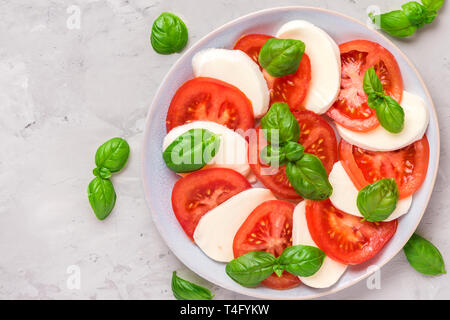 salad caprese with ripe tomatoes and mozzarella cheese, fresh basil leaves on concrete background. Italian food. top view with copy space. flat lay Stock Photo