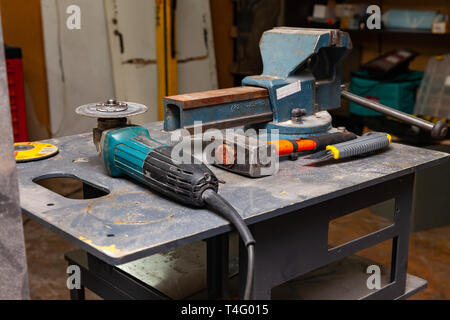 View of a workbench with a set of tools consisting of a large heavy vise, angle grinder, screwdriver, cutter, sledgehammer, and a spare cutting disc i Stock Photo