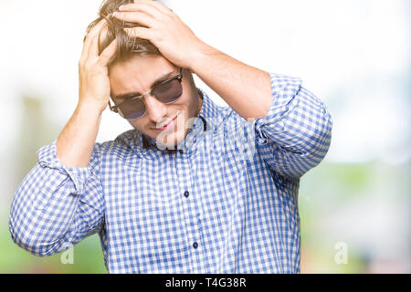 Young handsome man wearing sunglasses over isolated background suffering from headache desperate and stressed because pain and migraine. Hands on head Stock Photo