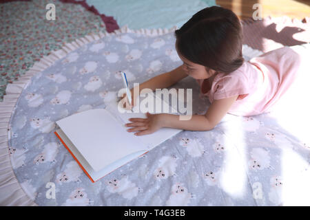 Child girl lies on the round mat and draws in album. Stock Photo