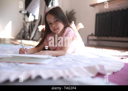 Child girl lies on the round mat and draws in album. Stock Photo