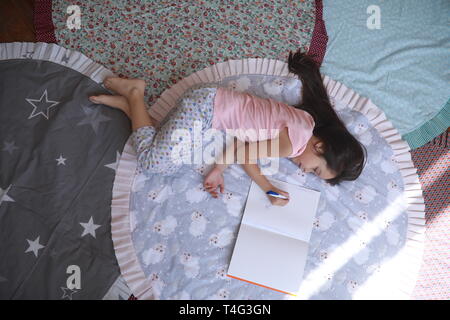 Child girl lies on the round mat and draws in album. Top view. Stock Photo