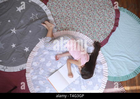 Child girl lies and sleeps on the round mat next to album. Top view. Stock Photo