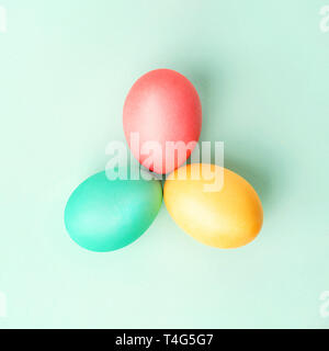 Three colorful handmade Easter eggs in triangle on mint colored background. Flat lay. Stock Photo