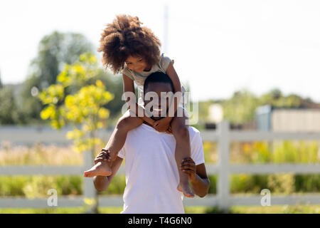 Smiling African American man carrying daughter on shoulders Stock Photo