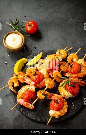 Grilled seafood. Delicious Grilled tiger shrimps with tomatoes, lemon and sauce served on a slate board. Seafood. Copy space. Stock Photo