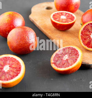 Whole and halved blood oranges on black surface, side view. Close-up. Stock Photo