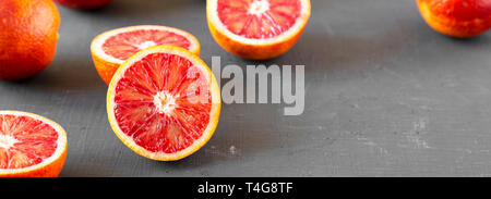 Whole and halved blood oranges on black surface, side view. Copy space. Stock Photo