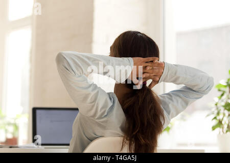 Woman relaxing on chair at work holding hands behind head Stock Photo